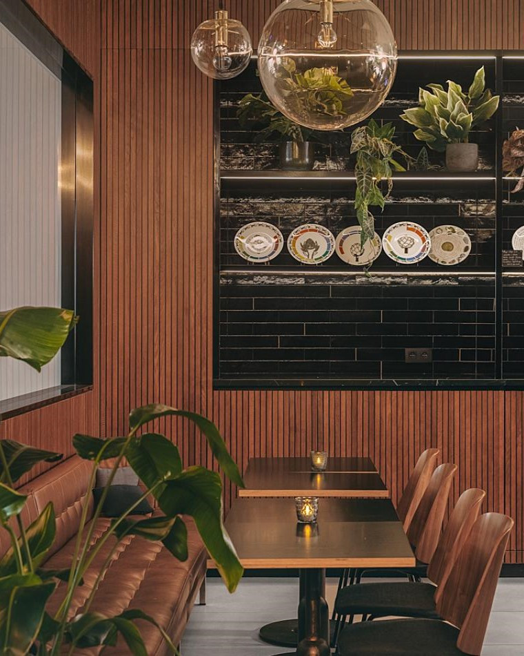 D-Bar en Drawing Lab, con plantas verdes y decoración sofisticada en tonos marrones y negros. 