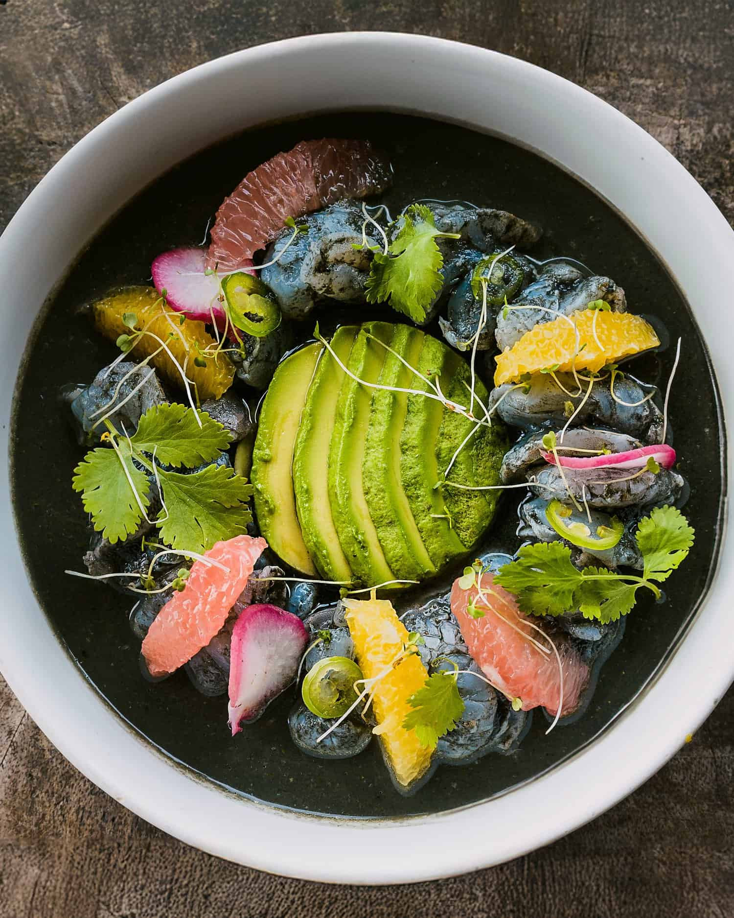Plato gastronómico y colorido con aguacate y frutas con una base negra de MVNGATA