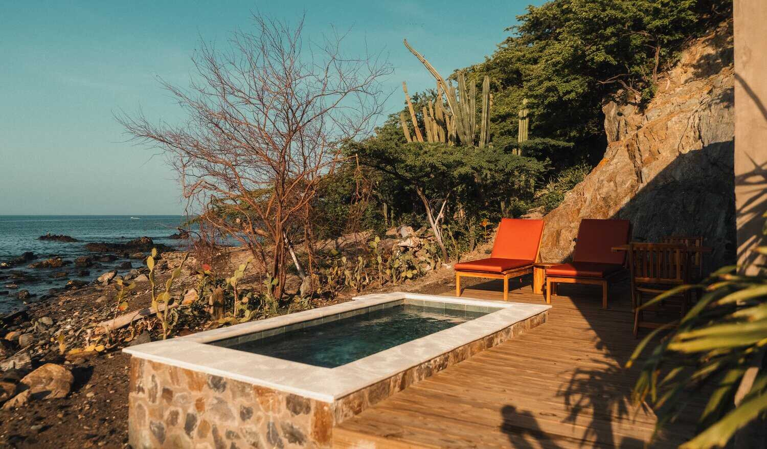 Piscina privada con tumbonas naranjas y vistas al mar en Perla Roca hotel boutique en Santa Marta