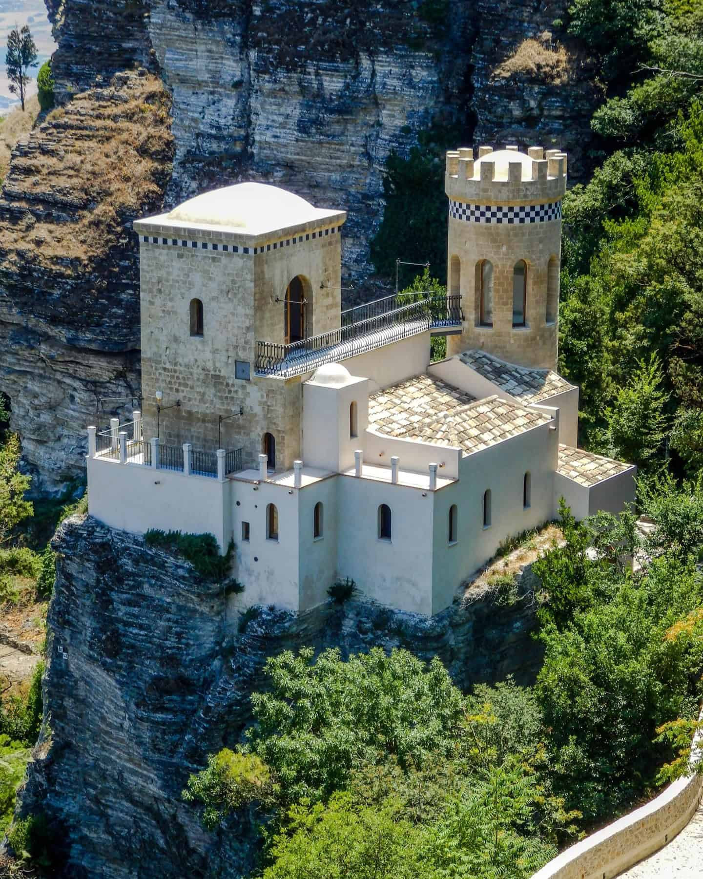 Castillo medieval sobre una piedra en un acantilado rodeado de arboles 