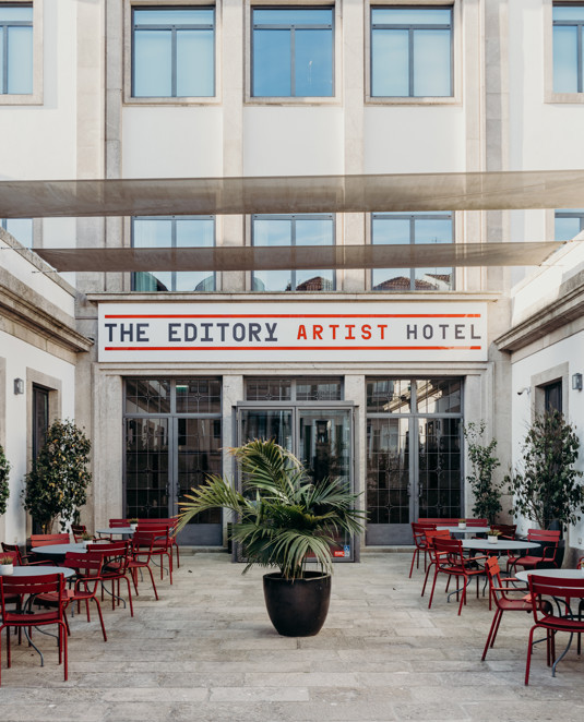 Entrance to The Editory Artist Baixa with red tables and chairs.